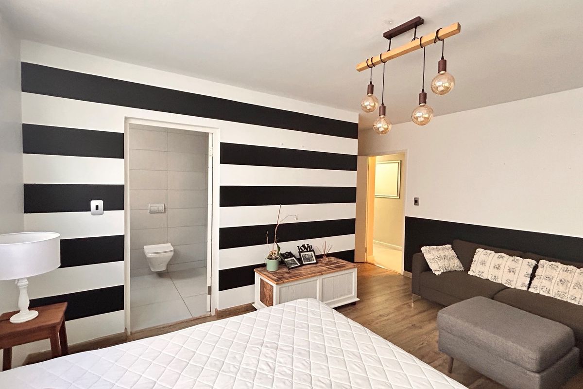 Bedroom featuring wood-look flooring, a modern pendant light fixture, and an en-suite bathroom with a wall-mounted toilet.