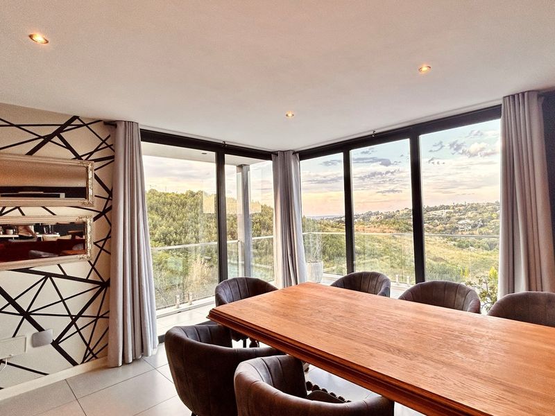 A bright dining area featuring floor-to-ceiling windows with scenic views, recessed lighting, and modern tiled flooring, creating an inviting space for meals.