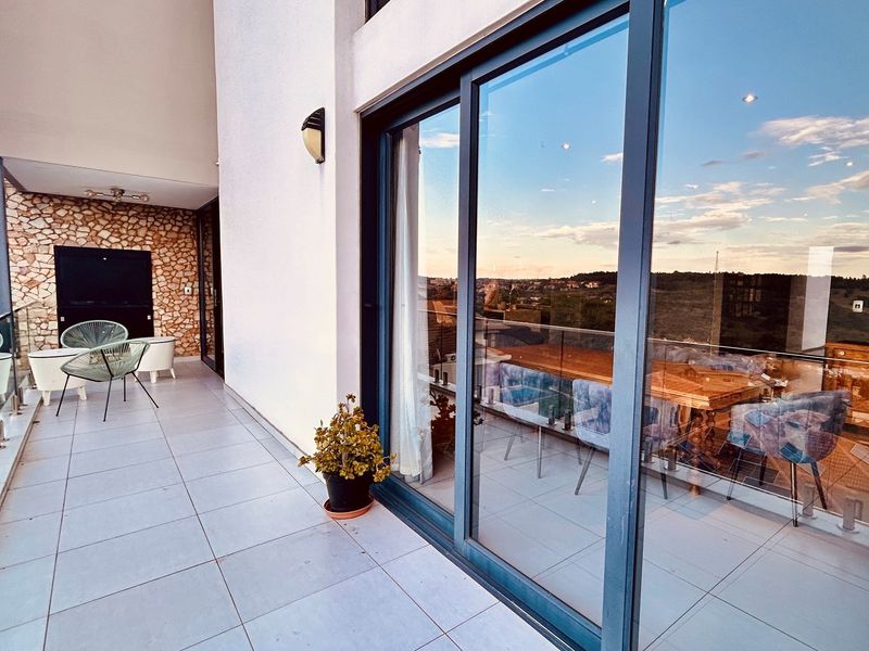 Spacious covered balcony featuring modern tiled flooring, a glass balustrade, and a decorative stone-clad feature wall, offering scenic views.