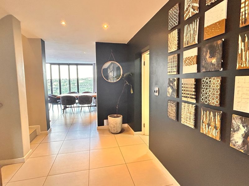 A bright, modern hallway featuring tiled flooring and recessed lighting, leading into an open-plan living and dining area with large windows.