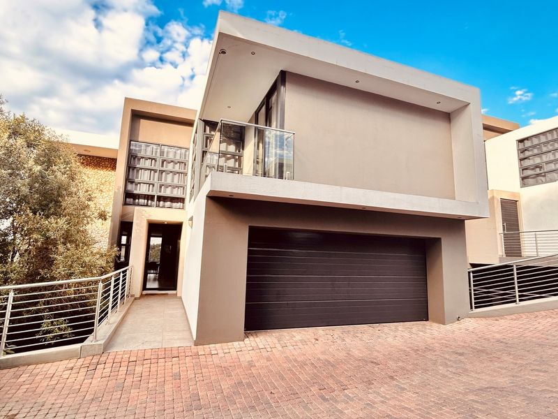 Modern townhouse exterior featuring a double garage, paved driveway, and an upper-level balcony with glass balustrades and contemporary stone cladding accents.