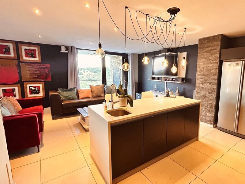 Modern open-plan living area featuring a central kitchen island with stone countertops, tiled flooring, and contemporary pendant lighting, seamlessly connecting to the lounge space.
