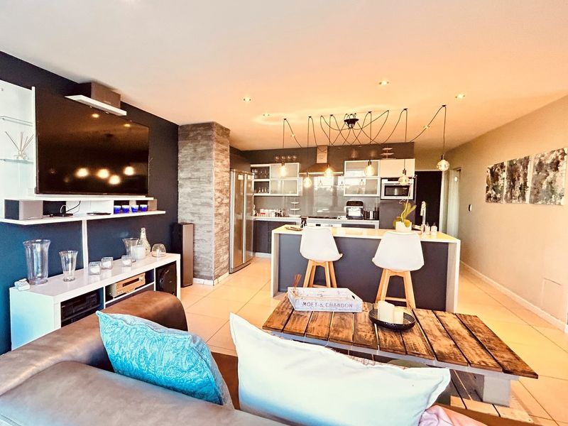 Spacious open-plan living area featuring a modern kitchen with a central island, stone feature pillar, and contemporary recessed lighting throughout.