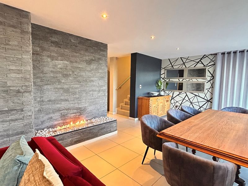 Spacious open-plan living and dining area featuring a striking stone-clad fireplace, modern tiled flooring, and recessed lighting, creating a contemporary and inviting atmosphere.