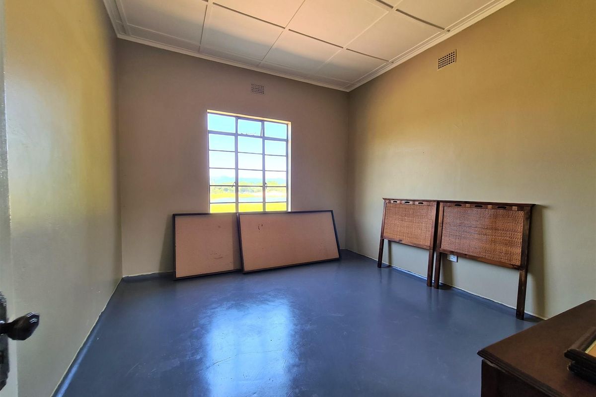 A spacious, empty bedroom featuring painted concrete flooring, a large multi-pane window, and a classic tiled ceiling.