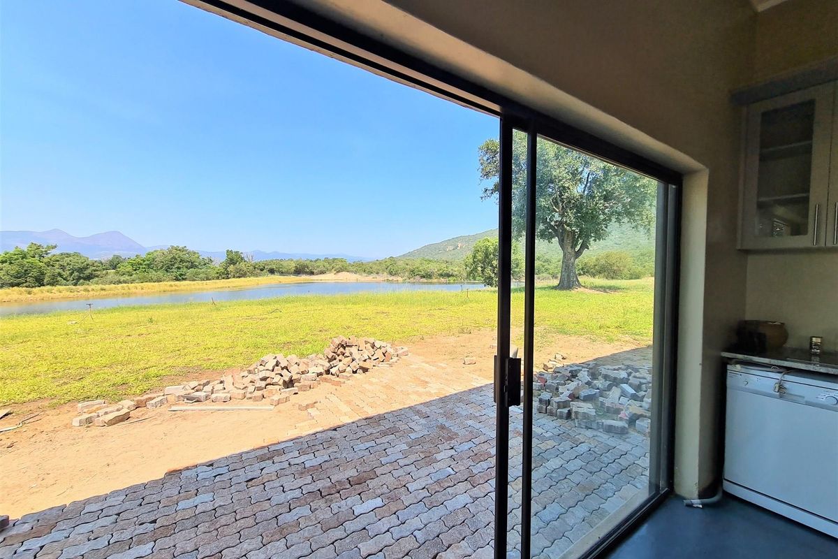 View from a living area through sliding glass doors onto a patio with unfinished paving and a scenic landscape featuring a pond.