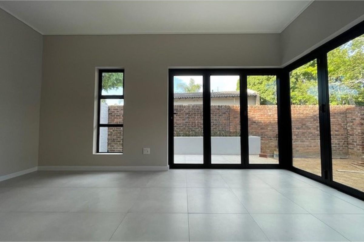 A bright, modern, and empty living area featuring large format floor tiles and black aluminium stacker doors opening to a private rear garden.
