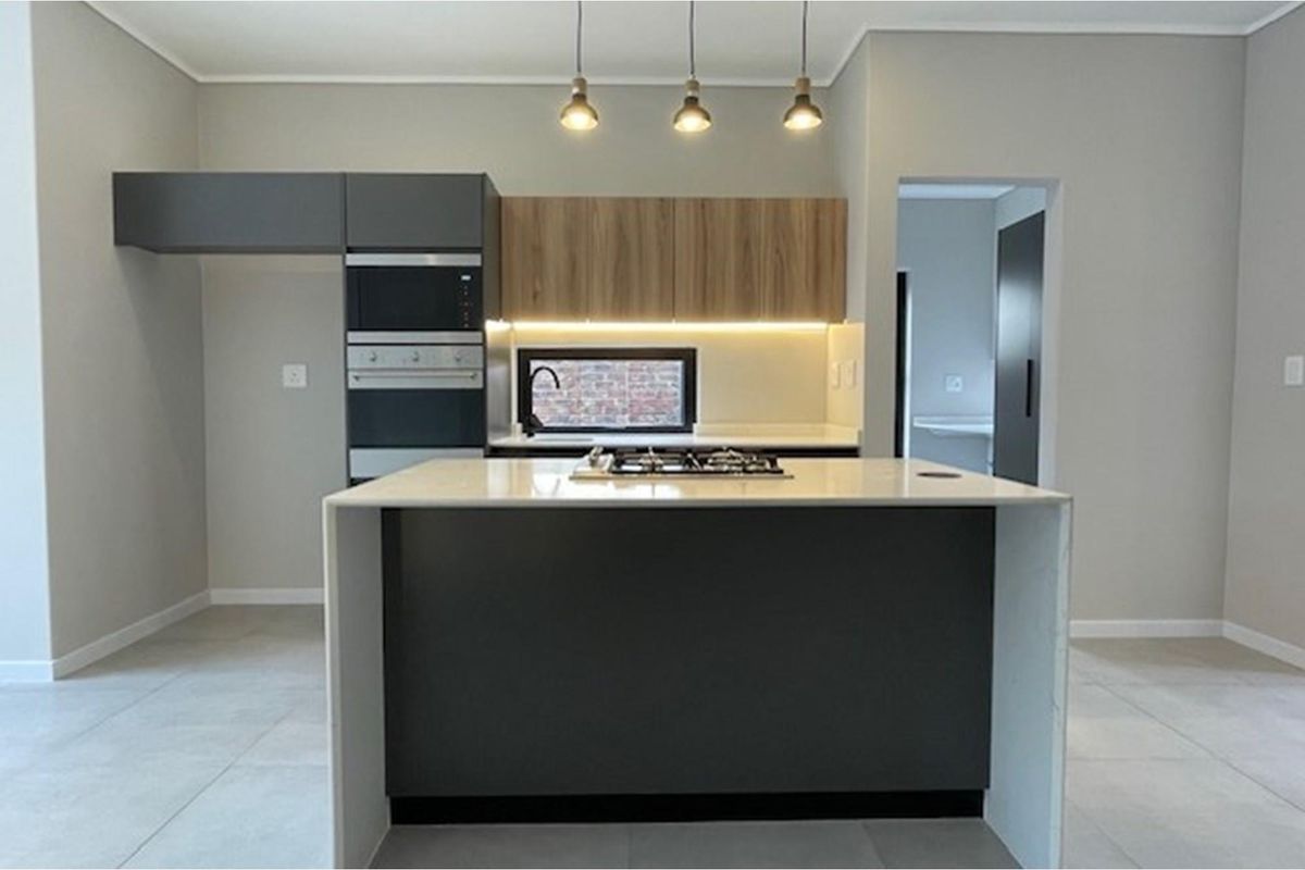 Modern kitchen featuring a central island with gas hob, built-in oven and microwave, stone countertops, and contemporary cabinetry with integrated lighting.