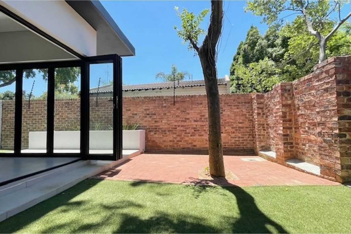 A private rear courtyard featuring a paved patio, artificial lawn, and exposed brick boundary walls with integrated electric fencing, accessible via bi-fold doors.