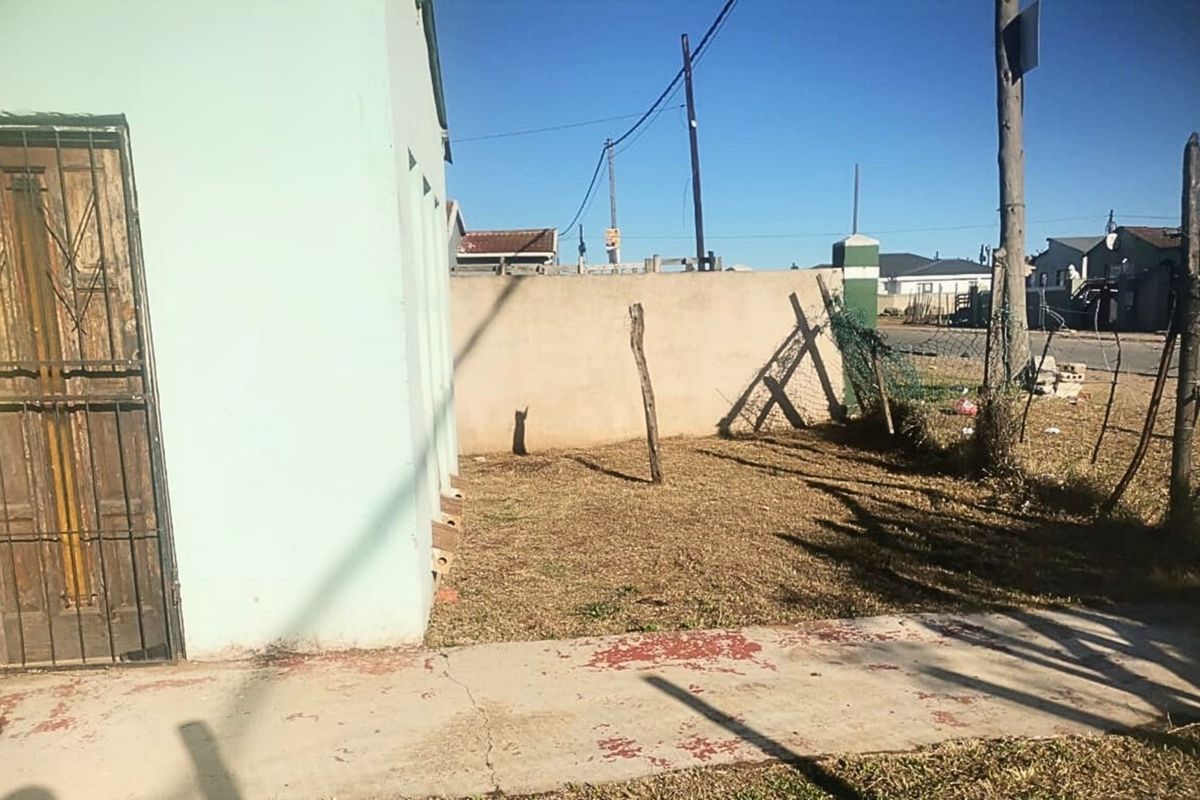 Exterior view of the property side yard featuring a concrete pathway, perimeter boundary wall, and damaged fencing.