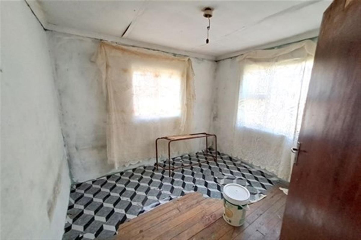 A bedroom space requiring significant renovation, featuring worn wall finishes, damaged ceiling panels, and mixed flooring materials.