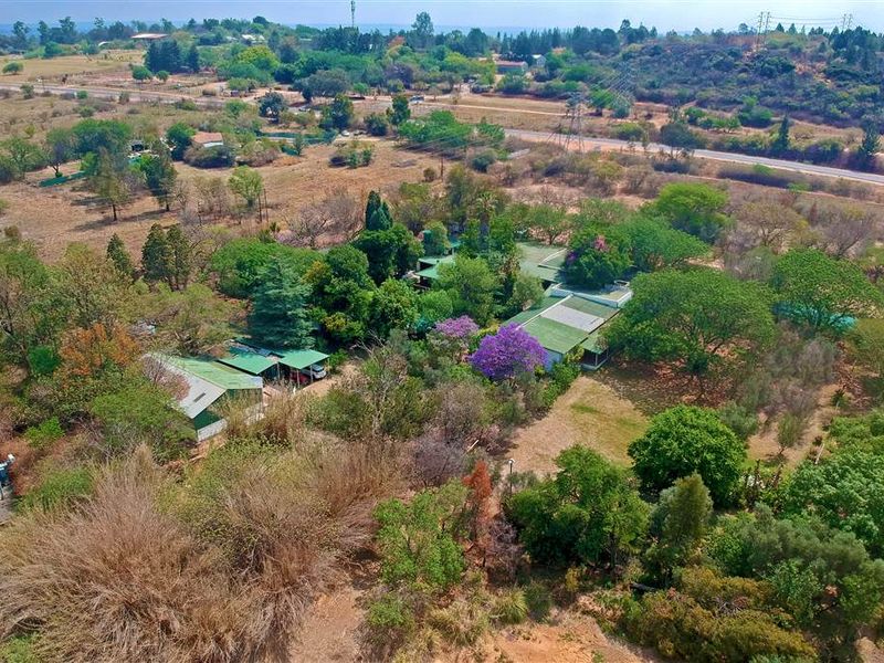 An aerial view of a large property featuring extensive landscaped gardens, mature trees, and multiple building structures with pitched roofs.
