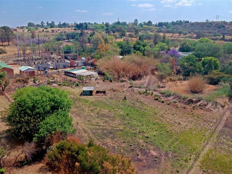 Aerial view of a large plot of land featuring an adjacent electrical substation, natural vegetation, and a small outbuilding structure.
