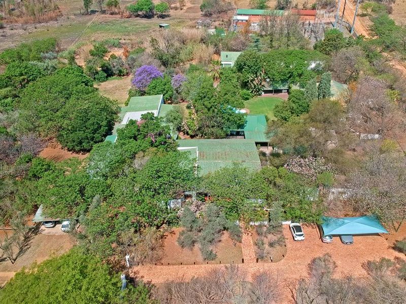 Aerial view of a large property featuring multiple buildings, extensive mature trees, a swimming pool, and covered parking areas.