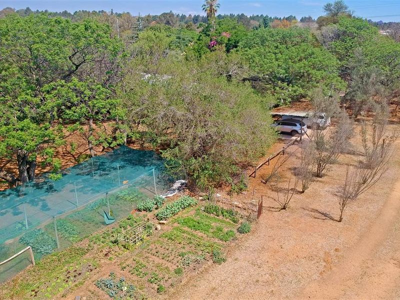 Aerial view of a large property featuring a vegetable garden with shade netting, mature trees, and a carport area.