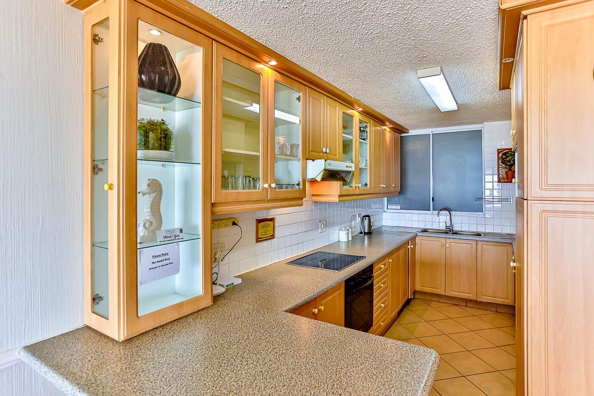 A functional kitchen featuring light wood cabinetry, tiled backsplash, integrated hob, and double sink with ample counter space.