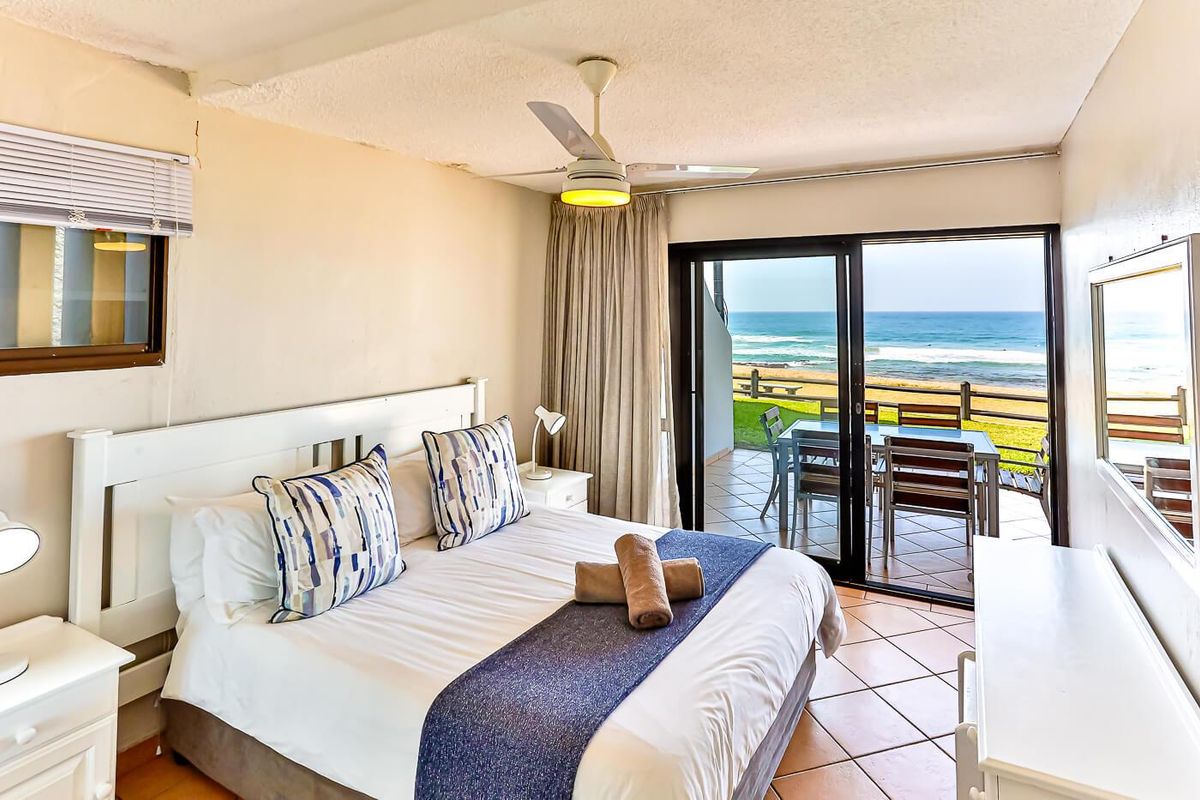 A bedroom featuring tiled flooring, a ceiling fan, and sliding glass doors that open onto a balcony with ocean views.