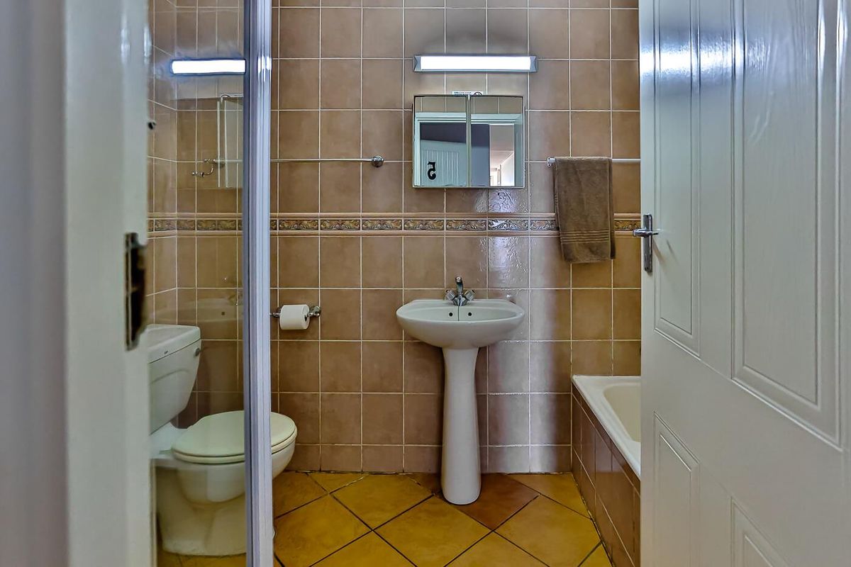 A functional bathroom featuring a pedestal basin, toilet, and bathtub with full-height wall tiling and tiled flooring.
