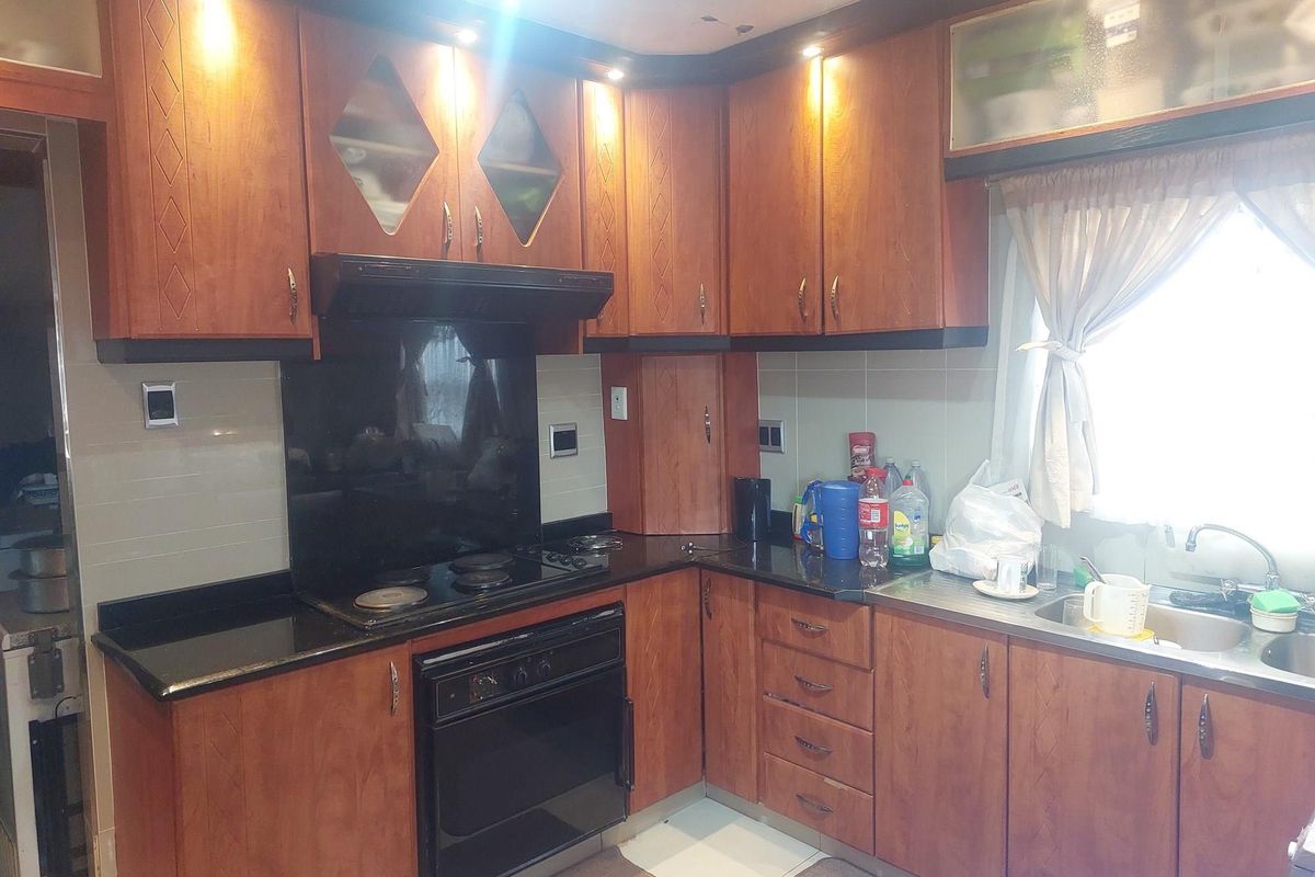 A functional kitchen featuring wood-finish cabinetry, black granite countertops, a built-in oven, and a stainless steel sink with tiled splashbacks.