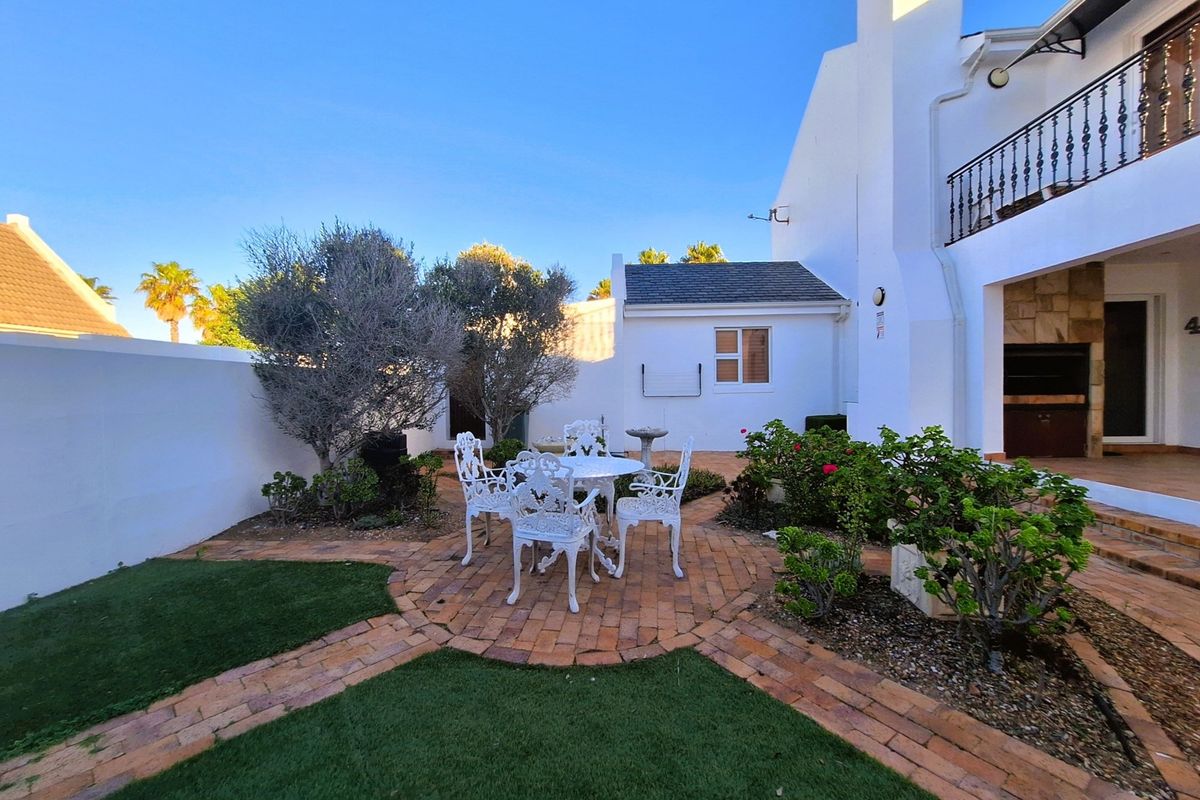 A well-maintained rear garden featuring a brick-paved patio area, manicured lawn, and a built-in outdoor braai area under a covered terrace.