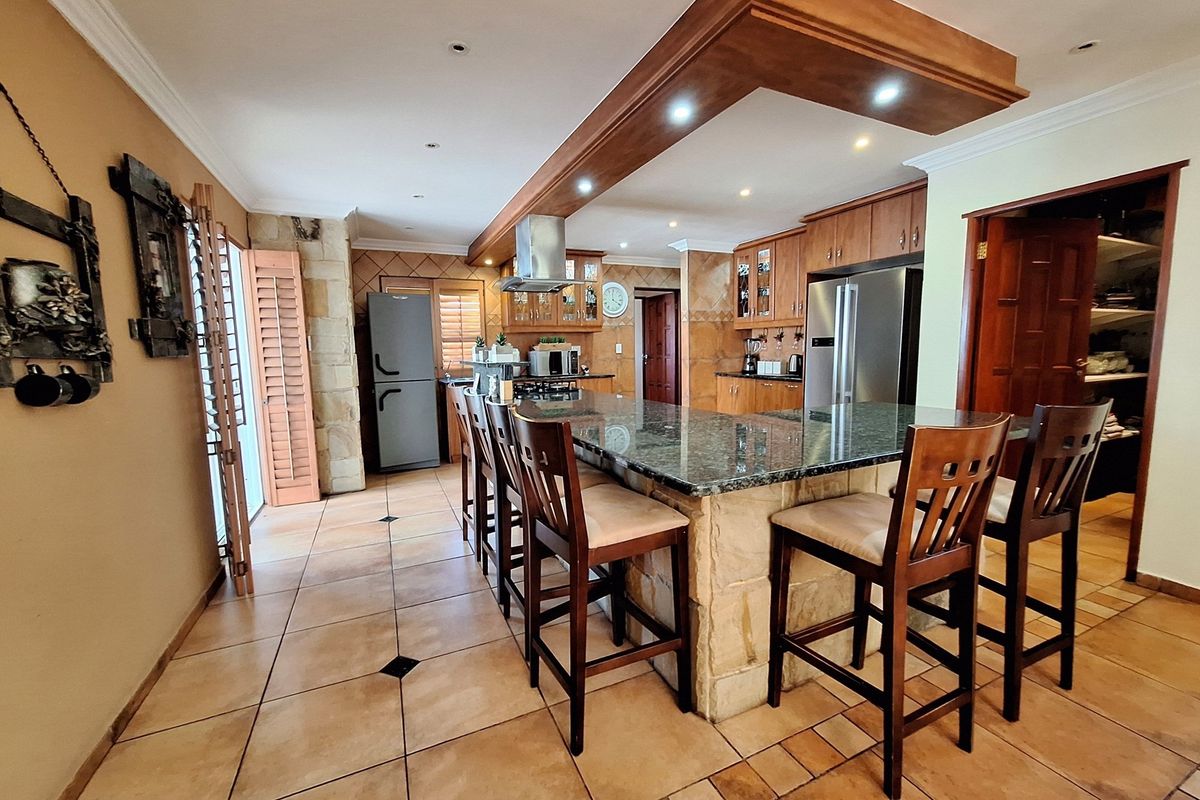 Spacious kitchen featuring a large granite-topped island, wooden cabinetry, stone cladding accents, and integrated lighting, providing a functional and warm culinary space.