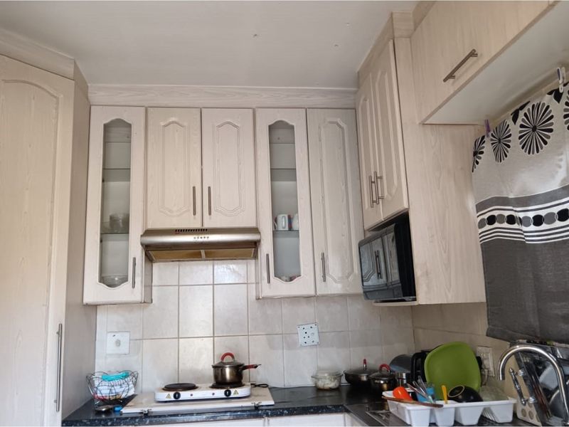 A functional kitchen area featuring light wood-grain cabinetry, a tiled backsplash, and integrated extractor fan above the cooking station.