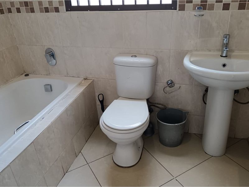 A functional bathroom featuring a built-in bathtub, pedestal basin, and toilet with neutral wall and floor tiling.