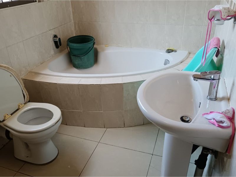 A functional bathroom featuring a corner bathtub, pedestal basin, and toilet with tiled walls and flooring.