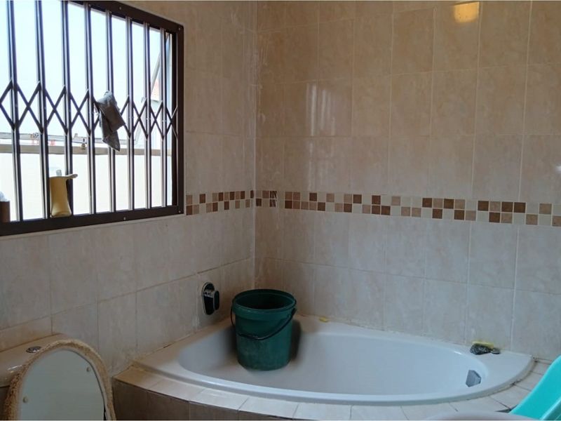 A bathroom featuring a built-in corner bathtub with tiled surround and a window fitted with security bars.