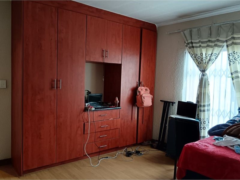 Bedroom featuring extensive built-in wooden cabinetry with integrated desk space and large window with security gate.