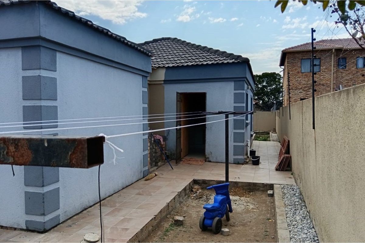 Rear exterior view showing a paved walkway, a metal washing line, and access to the rear of the house with perimeter walling.