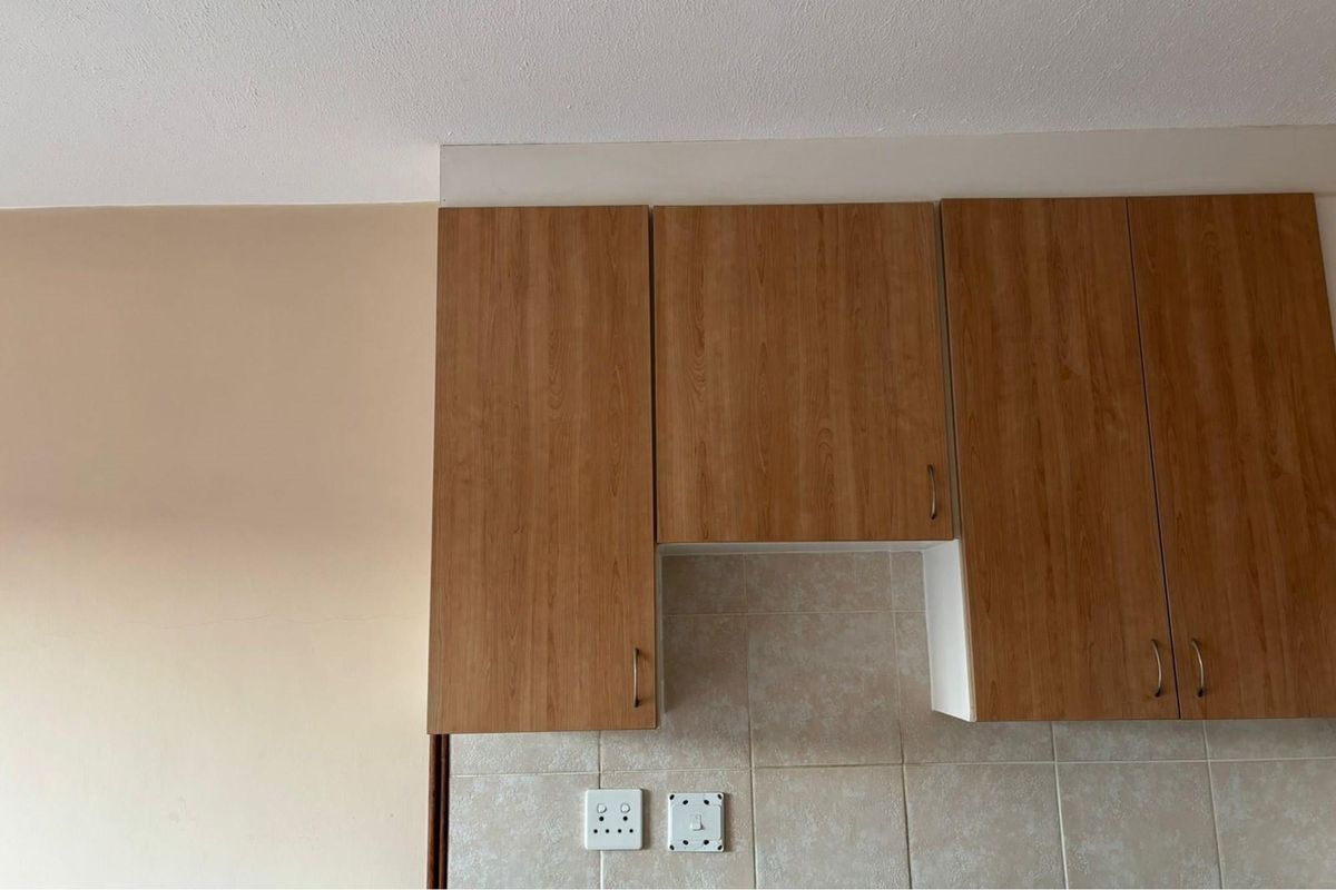 Close-up view of kitchen wall-mounted cabinetry with wood-look laminate finish and tiled splashback featuring integrated electrical outlets.