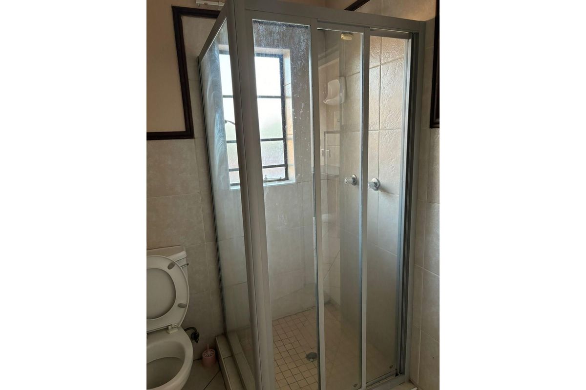 A functional bathroom featuring a corner shower enclosure with sliding glass doors and a standard toilet, finished with neutral wall tiling.