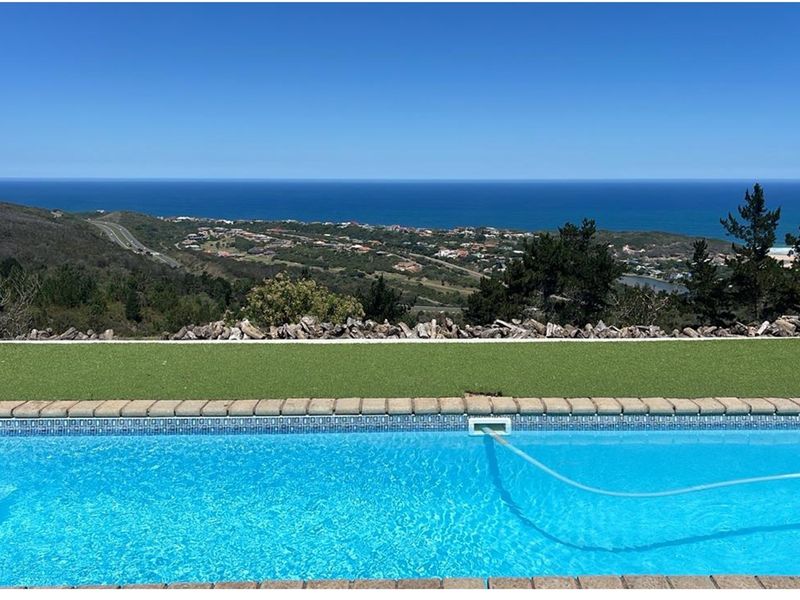 A swimming pool with a paved edge and artificial grass border, offering an expansive panoramic view of the coastline and surrounding landscape.