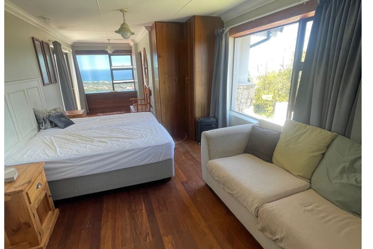 Spacious bedroom featuring timber flooring, built-in wooden wardrobes, and large windows offering scenic coastal views.