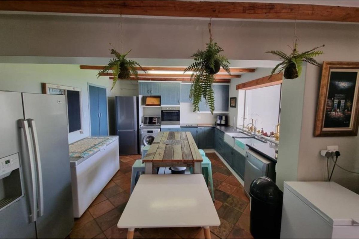 A rustic-style kitchen featuring blue cabinetry, exposed timber ceiling beams, terracotta floor tiles, and a farmhouse-style sink with integrated appliances.
