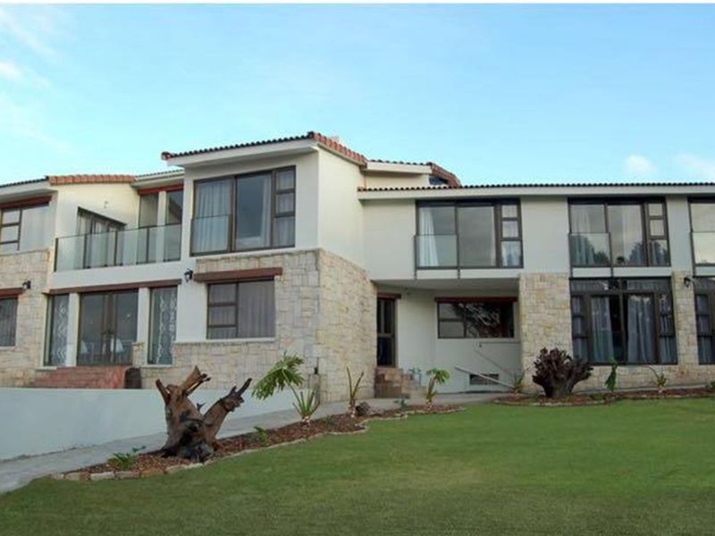 A spacious two-story residential property featuring stone cladding, large glass sliding doors, and balconies overlooking a well-maintained garden.
