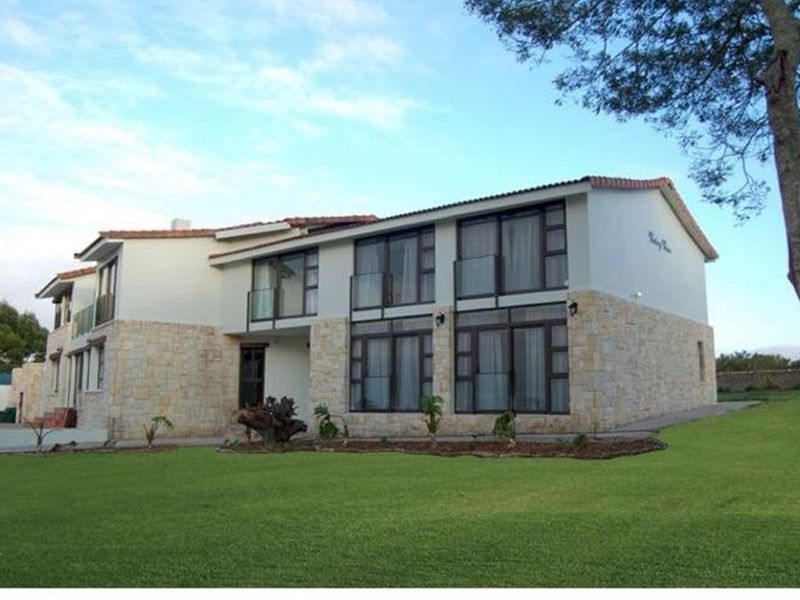 A two-story residential building featuring stone cladding, large glass sliding doors, and balconies, set within a well-maintained garden.