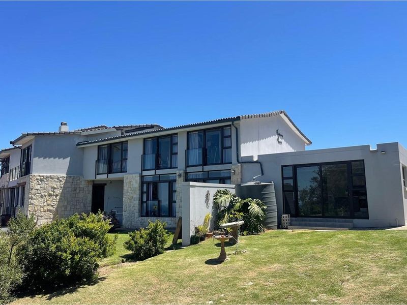 A modern two-story residential exterior featuring stone cladding, large dark-framed windows, and a spacious lawn area with a water tank.