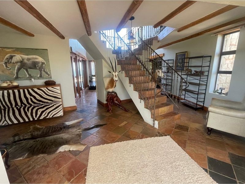 Spacious entrance hall featuring terracotta floor tiles, exposed timber ceiling beams, and a central staircase with decorative wrought iron balustrades.