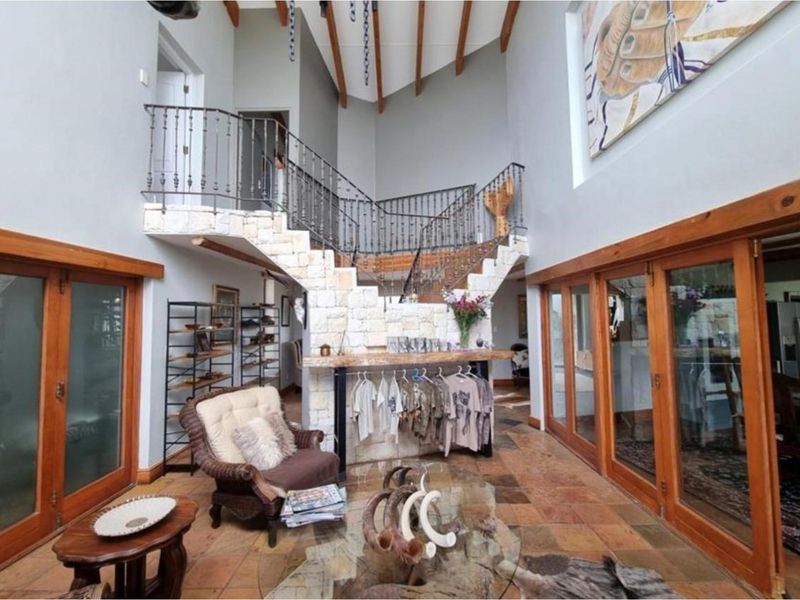 Spacious double-volume entrance hall featuring a stone-clad staircase with wrought iron balustrades, terracotta tiled flooring, and large timber-framed glass doors.