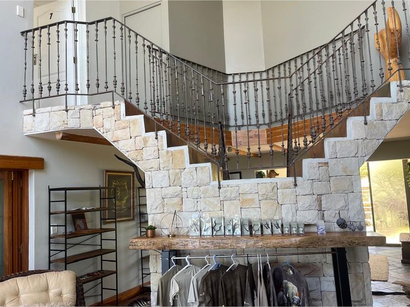 A grand entrance hall featuring a prominent stone-clad staircase with decorative wrought iron railings and a natural timber accent shelf.