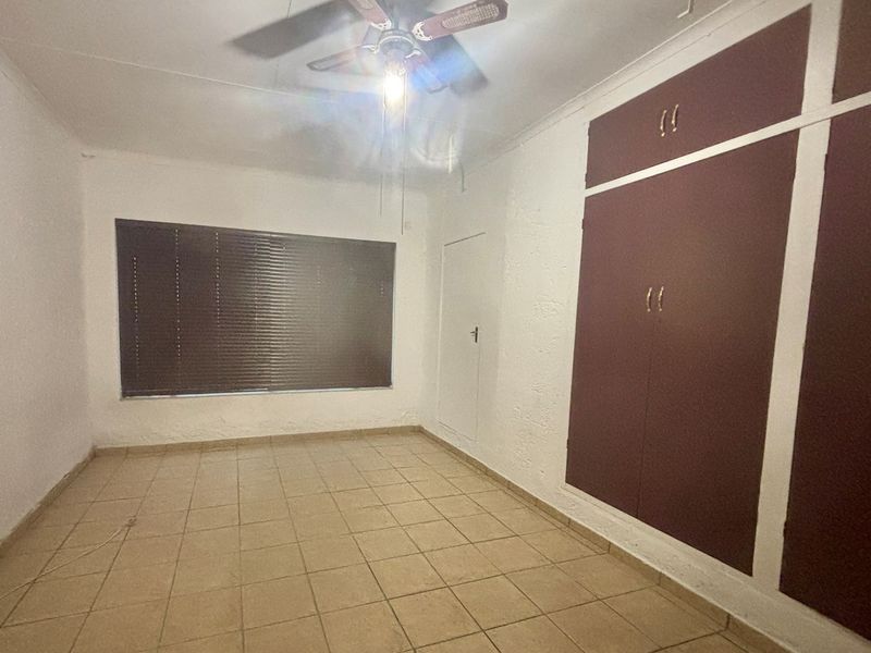 An empty bedroom featuring tiled flooring, a ceiling fan, and built-in cupboards with a dated finish.