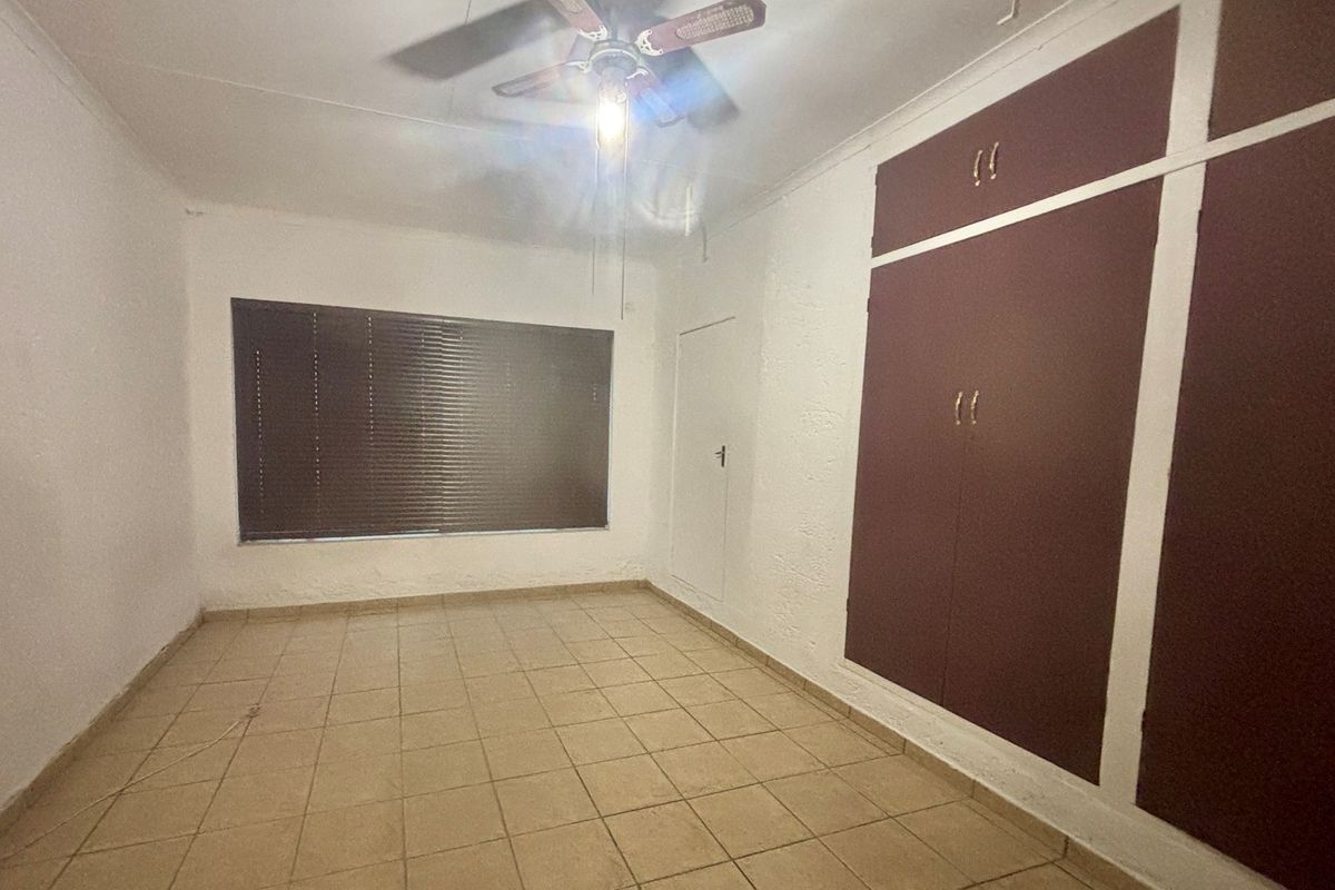 An empty bedroom featuring tiled flooring, a ceiling fan, and built-in cupboards with a dated finish.