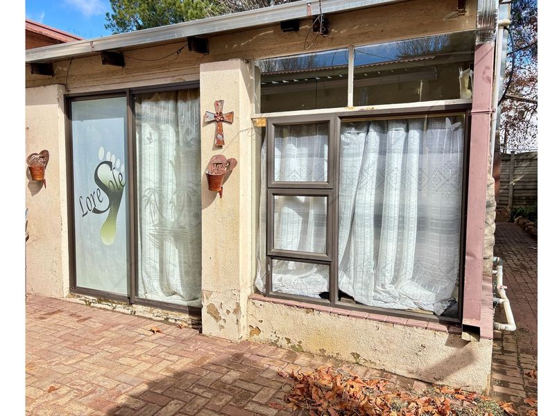 Rear exterior view of the apartment featuring brick paving, sliding glass doors, and aluminium window frames with visible wear to the exterior plaster finish.