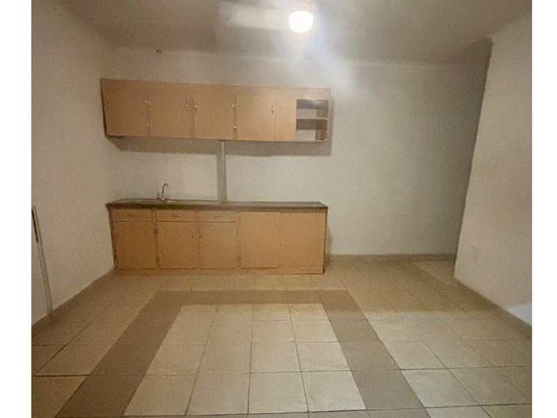 A basic, empty kitchen area featuring dated built-in cabinetry, a sink, and tiled flooring, offering potential for a modern renovation.
