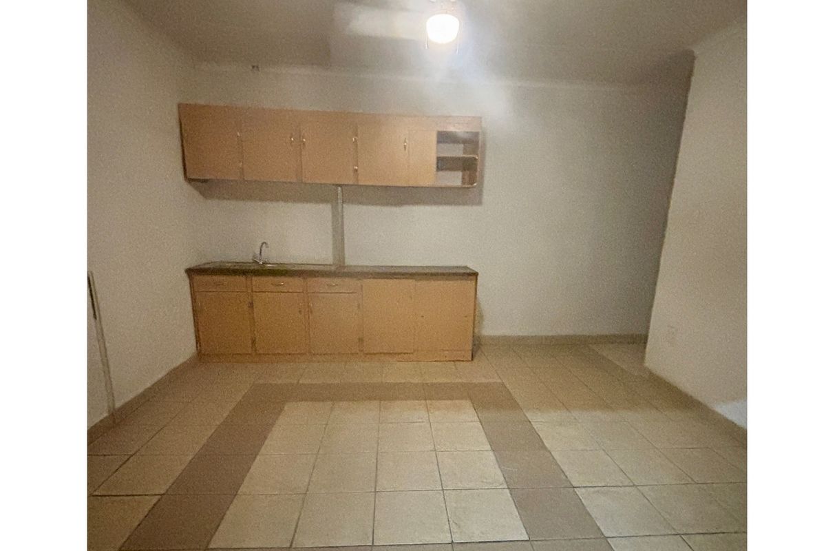 A basic, empty kitchen area featuring dated built-in cabinetry, a sink, and tiled flooring, offering potential for a modern renovation.