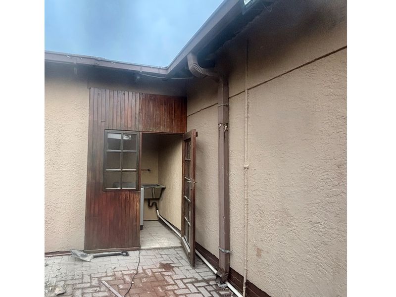 Rear exterior view of the property featuring a paved courtyard, utility sink area, and weathered timber cladding.