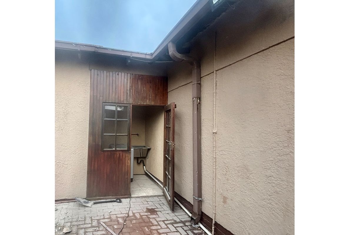 Rear exterior view of the property featuring a paved courtyard, utility sink area, and weathered timber cladding.