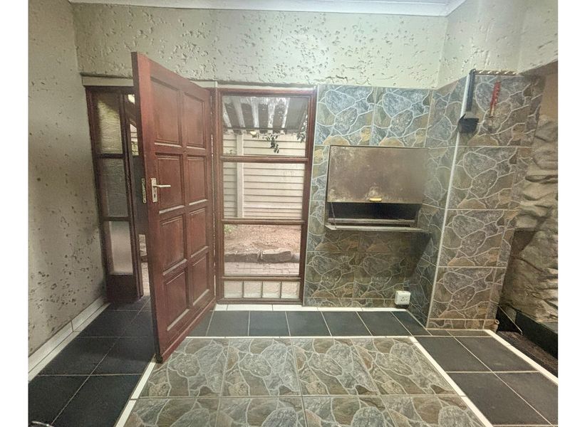 Covered patio area featuring a built-in braai, tiled flooring, and direct access to the exterior through a timber and glass door.
